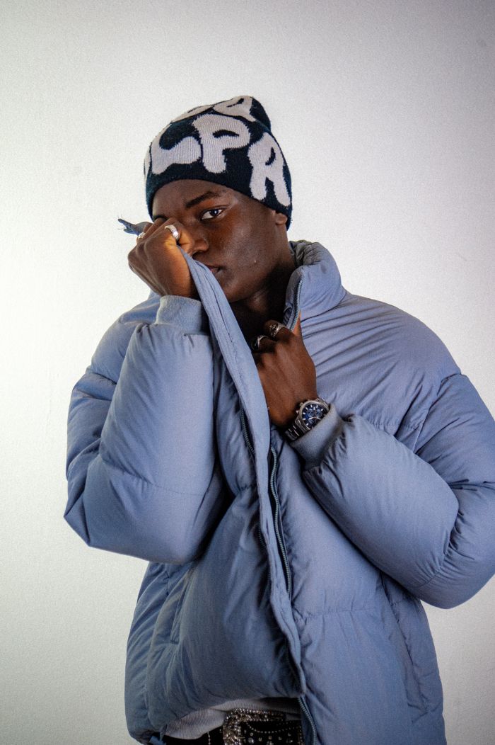 Home Stylish young man wearing a blue puffer jacket and knit hat in a studio portrait.