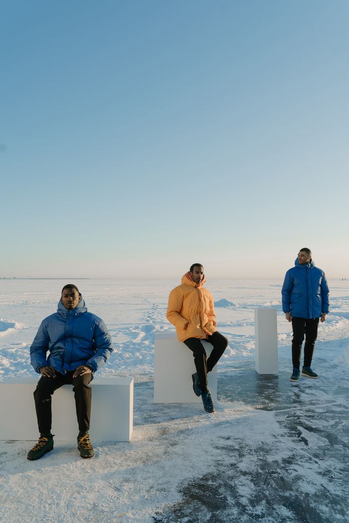 Services Three men in colorful puffer jackets pose on a snowy landscape under a clear blue sky.